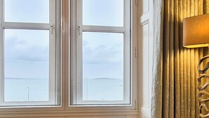 A room with a large window overlooking a body of water, a wall-mounted lamp, and wooden paneling.