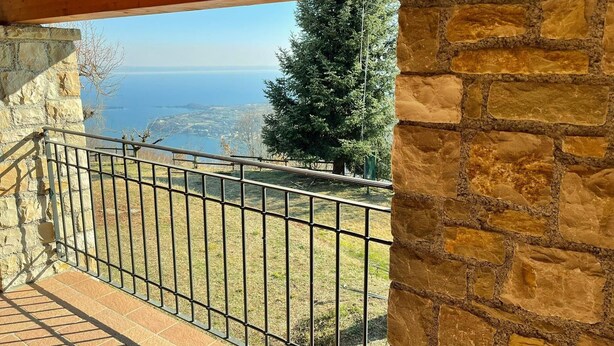 A balcony with a stone wall, metal railing, and a view of a body of water and trees.