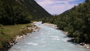 A river flowing through a mountainous area with rocky banks and dense greenery on both sides.