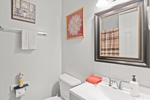 A bathroom with a toilet, sink, towel rack, and framed artwork on the wall.