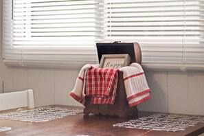 A dining table with placemats, a wooden chest with a 'Happy' sign, and a plaid blanket.