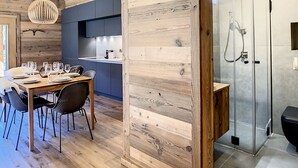 Eine moderne Küche mit Holzakzenten, ein Essbereich mit Holztisch und -stühlen sowie eine Dusche mit Glasabtrennung.