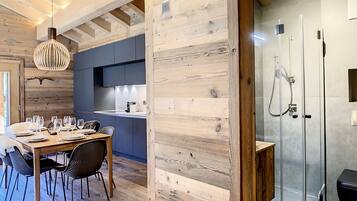 A modern kitchen with wooden accents, a dining area with a wooden table and chairs, and a glass-enclosed shower area.