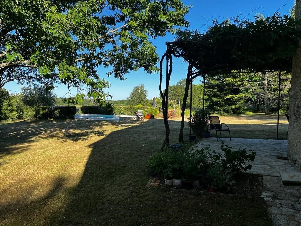A backyard with a grassy lawn, a wooden pergola, and a stone patio area.