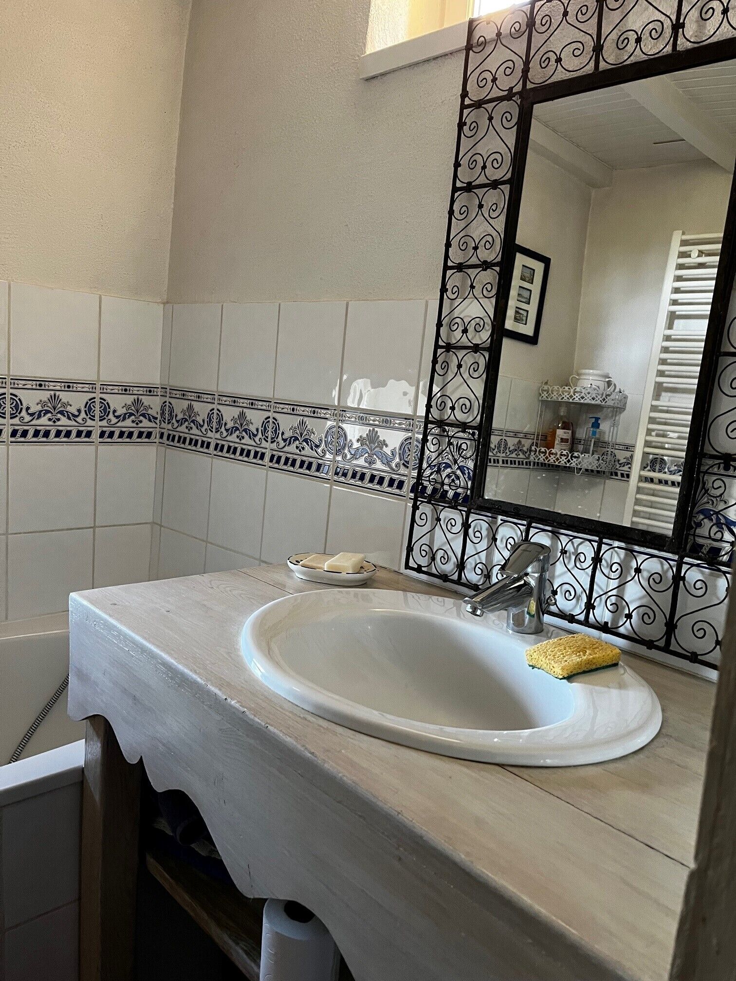 Une salle de bain avec un lavabo blanc, un miroir doté d’un cadre décoratif et un mur recouvert de carreaux.