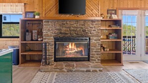 Una chimenea de piedra con un televisor encima, estantes de madera y vistas al exterior.