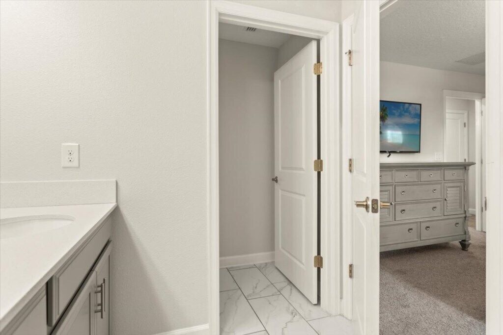 A bathroom with a white sink, a door leading to another room, and a television in the background.