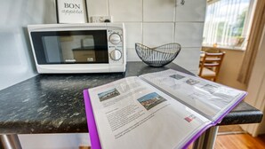 A kitchen with a microwave, a framed sign, a black bowl, and a magazine on the counter.