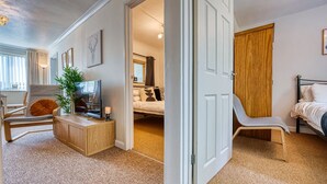 A room with a bed, a desk, a chair, a TV, and a door leading to another room.