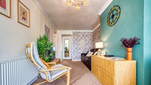 A living room with a chair, a wooden cabinet, a clock, and a plant.