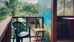 A wooden deck with a chair and a small table, overlooking a lush green landscape. - Hidden Jungle Beach House, a Unique Guesthouse in Puerto Viejo de Talamanca!  (Puerto Viejo de Talamanca)