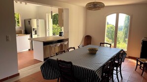 Een eetruimte met een tafel en stoelen, een keuken op de achtergrond en uitzicht door een glazen deur.