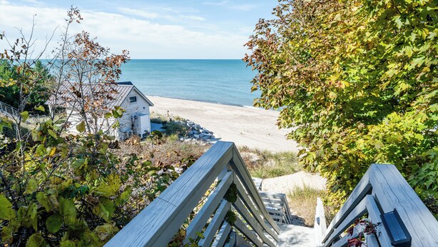 Un escalier en bois mène à une plage, avec une maison visible au loin.
