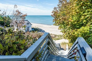 A wooden staircase leading to a beach with a house in the background. - 2027 NOW OPEN! New Buffalo Lakefront Home With Private Beach and Hot Tub! (New Buffalo)