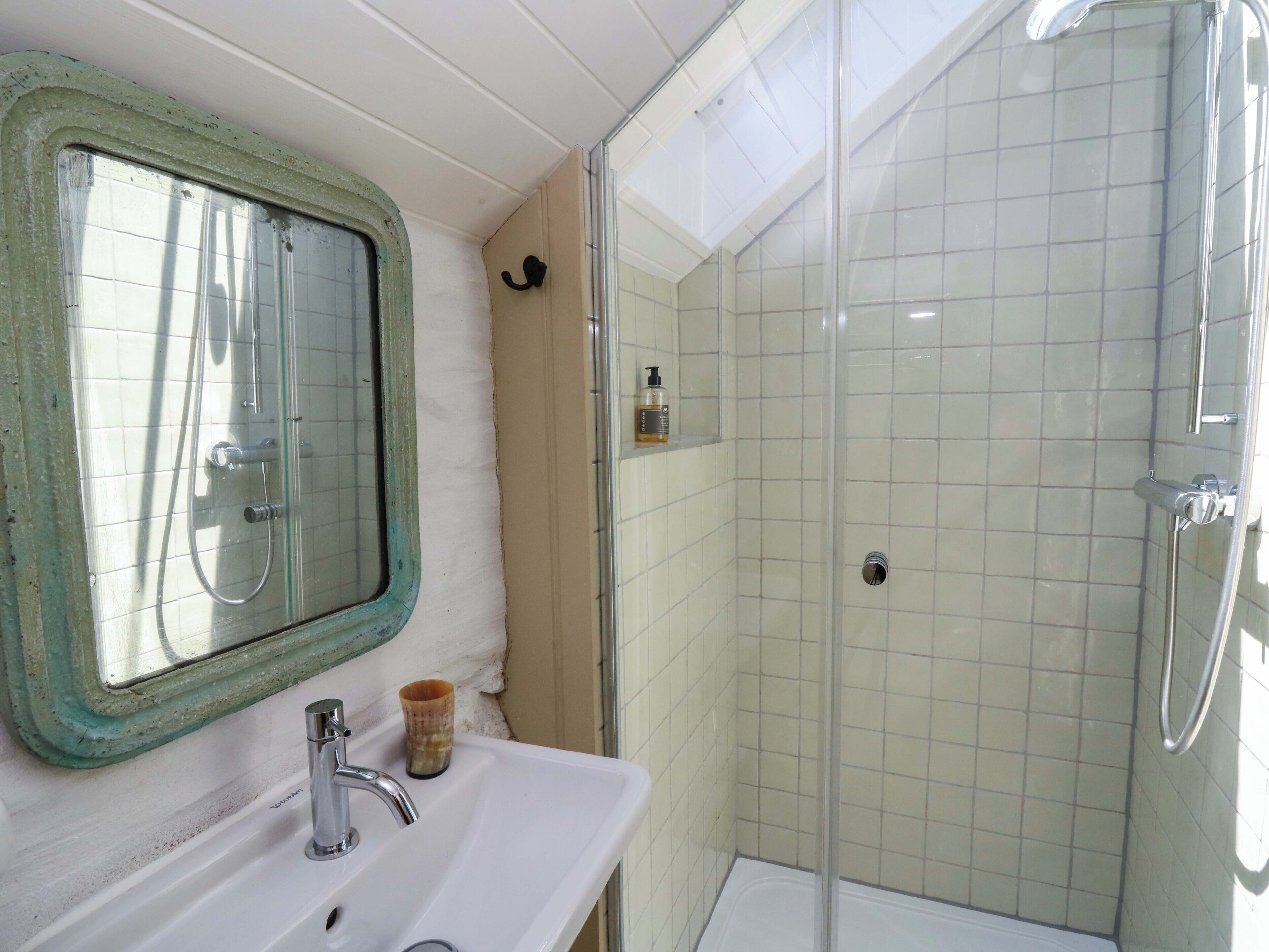 A bathroom with a white sink, a mirror with a green frame, a glass shower enclosure, and a small shelf with toiletries.