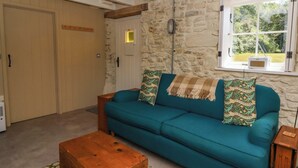 A cozy living room with a teal sofa, a wooden coffee table, and a stone wall. - Dolwylan Barn (Llandysul)