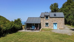 A stone house with a blue door and a covered porch with outdoor seating. - Dolwylan Barn (Llandysul)