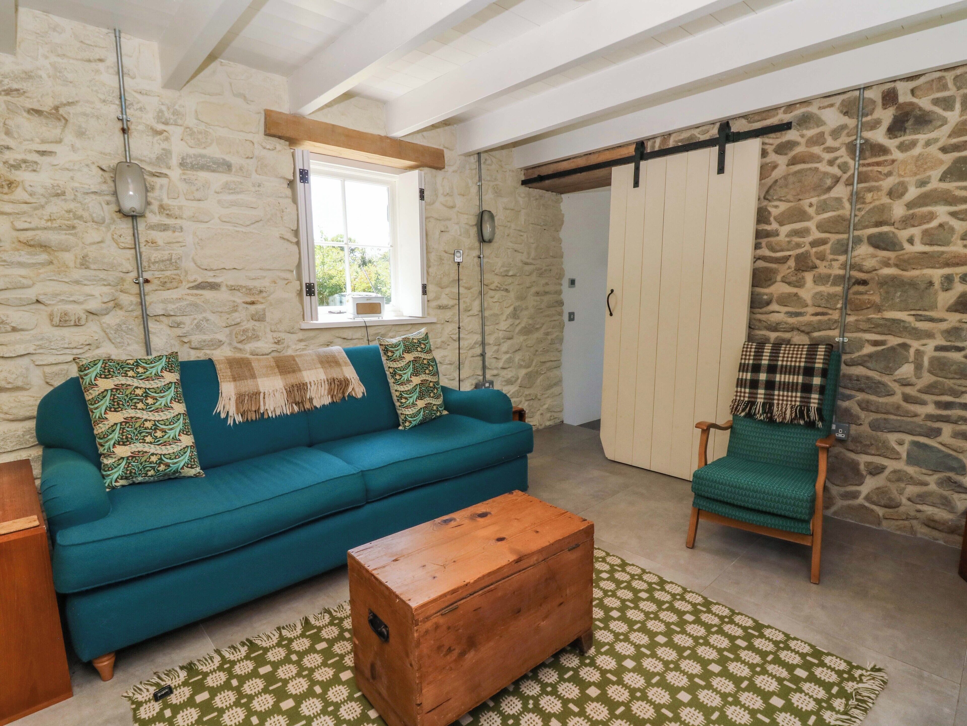 Una sala de estar acogedora con un sofá azul verdoso, un cofre de madera y un tapete estampado verde.