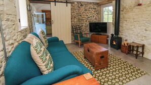 A cozy living room with a stone wall, a green sofa, a wooden coffee table, a TV, and a fireplace. - Dolwylan Barn (Llandysul)