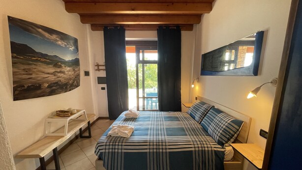A bedroom with a bed, a bench, a painting, a window with curtains, and a wall-mounted lamp. - BLU Flat (2 pax) + 2 Bunks Bed, FIOCCHINA magic place - Salò - Garda Lake (Lombardia)