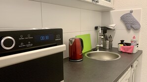 A kitchen with a digital clock displaying 08:38, a kettle, a green cutting board, a sink with utensils, and a pink towel. - Apartment 1, centrally located on the waterfront (Emden)