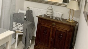 A small, neatly arranged room with a white radiator, a wooden cabinet with a mirror above it, a lamp, and a table with a chair. - Apartment 1, centrally located on the waterfront (Emden)