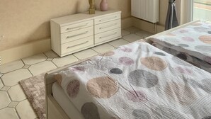 A bedroom with two beds, a dresser, a radiator, and a window with curtains. - Apartment 1, centrally located on the waterfront (Emden)