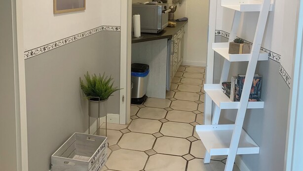 A hallway with a tiled floor, a small plant, a trash bin, and a white shelf unit. - Apartment 1, centrally located on the waterfront (Emden)