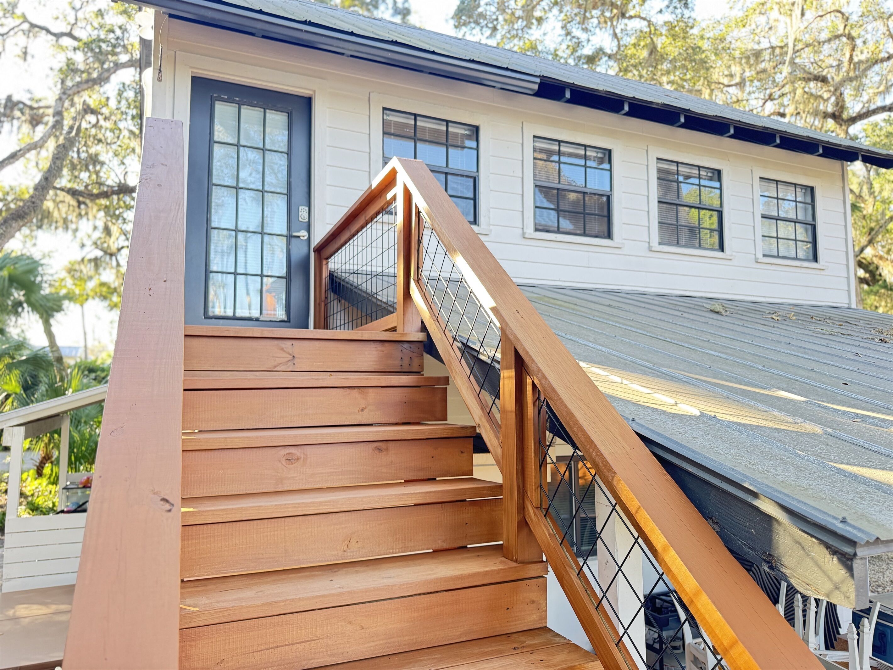 Un escalier en bois mène à une maison blanche dotée de nombreuses fenêtres et d’un toit en métal.