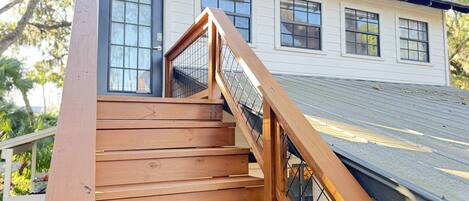 Un escalier en bois mène à une maison blanche dotée de nombreuses fenêtres et d’un toit en métal.