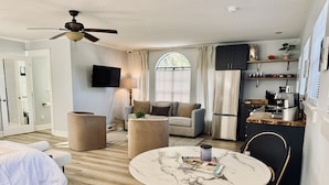 A compact living space with a bed, a round table, a sofa, a ceiling fan, a kitchen area with a refrigerator, and a TV mounted on the wall. - Guesthouse/TPC/GuanaViews/WalkBeach/HotTub (Ponte Vedra Beach)