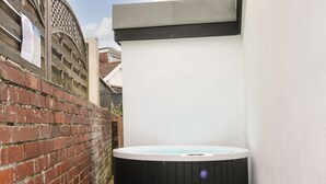 A hot tub in a backyard with a brick wall and a white fence. - Sunnydene (Paignton)