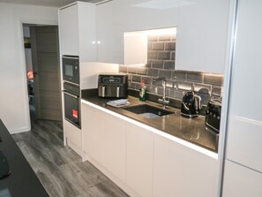 A modern kitchen with white cabinets, a black countertop, a built-in oven, a coffee maker, and a sink. - Sunnydene (Paignton)