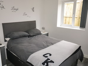 A bedroom with a bed, a nightstand, a bedside table, a window, and wall decorations.