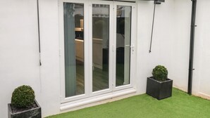 A white exterior wall with a sliding glass door, a tiled roof, and two potted plants. - Sunnydene (Paignton)