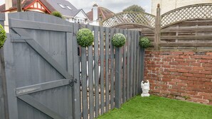 A wooden gate with a latch, a brick wall, and a small white statue in a grassy area. - Sunnydene (Paignton)