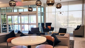 A modern lounge area with a round table, comfortable seating, and large windows offering a view of the outdoors. - La Quinta Inn & Suites By Wyndham Pflugerville (Pflugerville)
