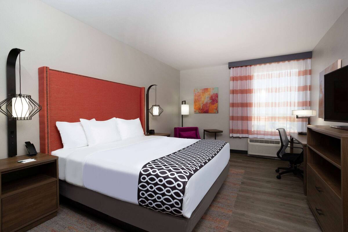A hotel room with a large bed, a desk, a chair, a TV, and a window with curtains.