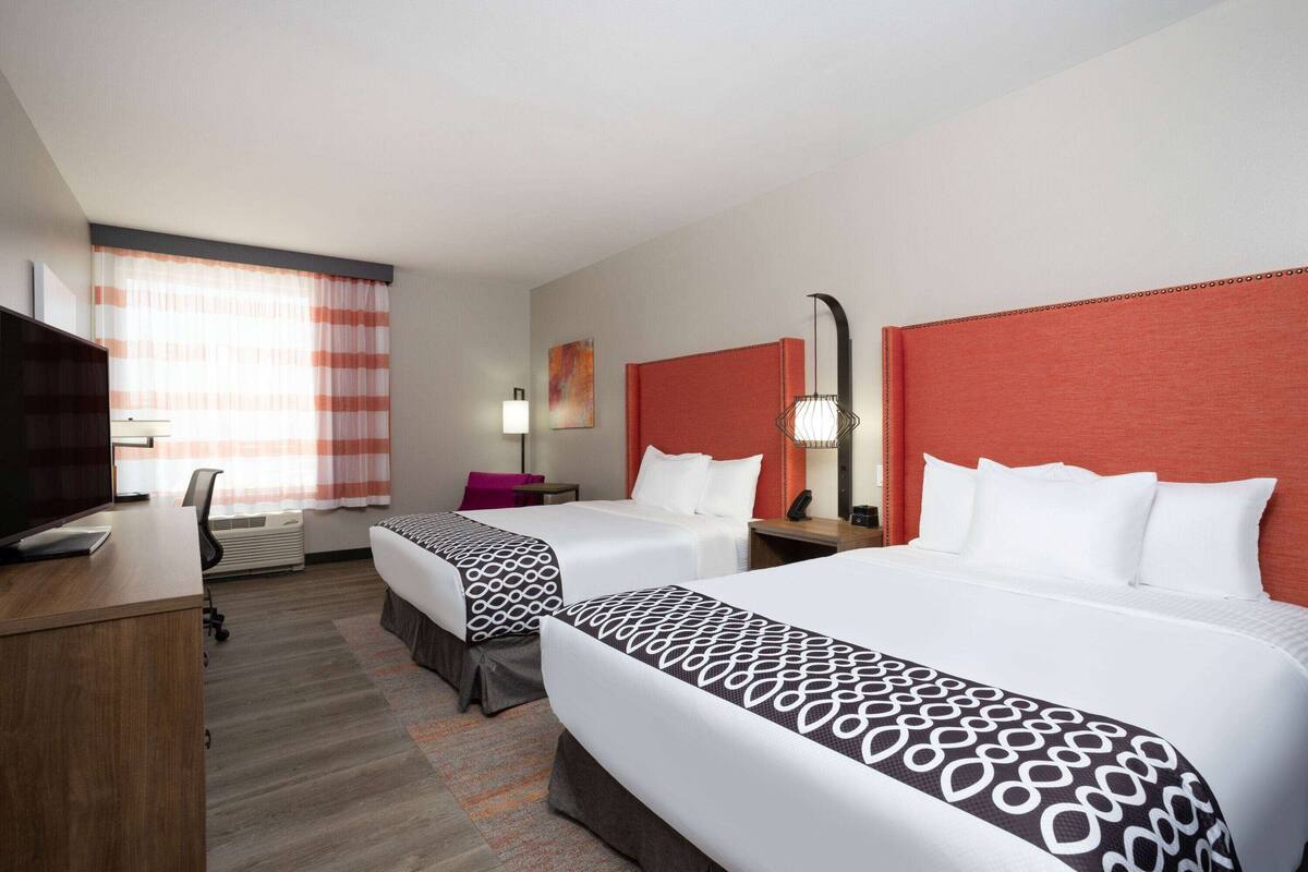 A hotel room with two beds, a desk, a chair, a TV, and a window with curtains.