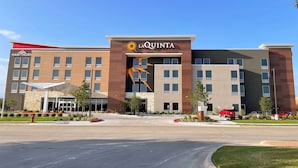 A modern hotel with a prominent 'La Quinta' sign, a 'Hawthorn' sign, and a large sun graphic on the facade. - La Quinta Inn & Suites By Wyndham Pflugerville (Pflugerville)