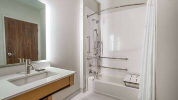 Un baño moderno con lavamanos, espejo y bañera blancos.