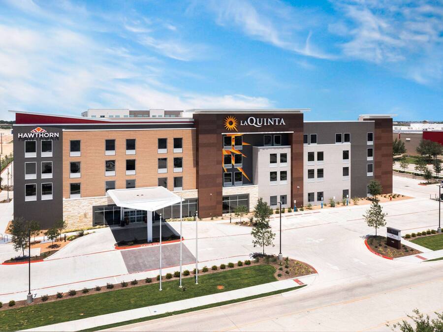 A modern hotel with a central entrance, multiple floors, and a parking area.