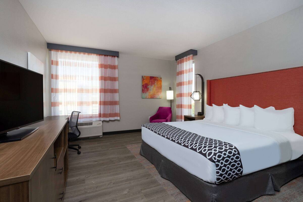 A hotel room with a bed, a desk with a TV, a chair, and a window with curtains.