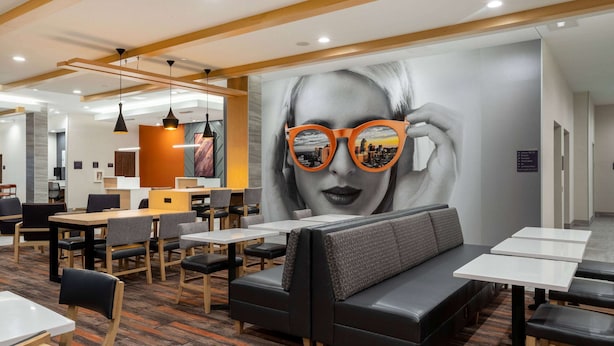 A modern restaurant with a large mural, seating areas, and pendant lighting. - La Quinta Inn & Suites By Wyndham Pflugerville (Pflugerville)