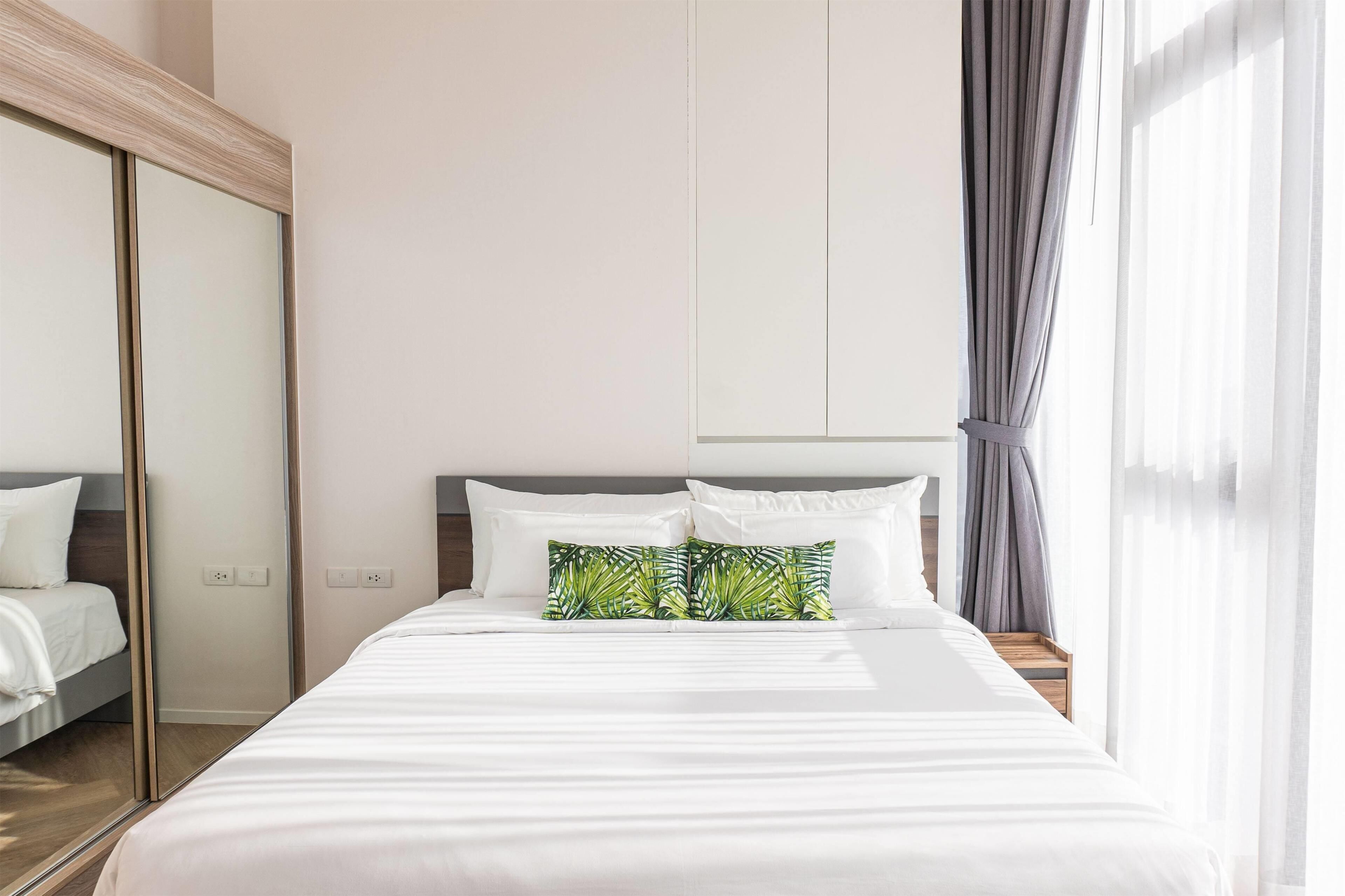 Habitación de hotel con una cama grande, un espejo, un armario y una ventana con cortinas.
