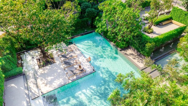 An aerial view of a swimming pool surrounded by lush greenery and a wooden deck with lounge chairs. - Ramada by Wyndham Bangkok Sukhumvit 87 (Bangkok)