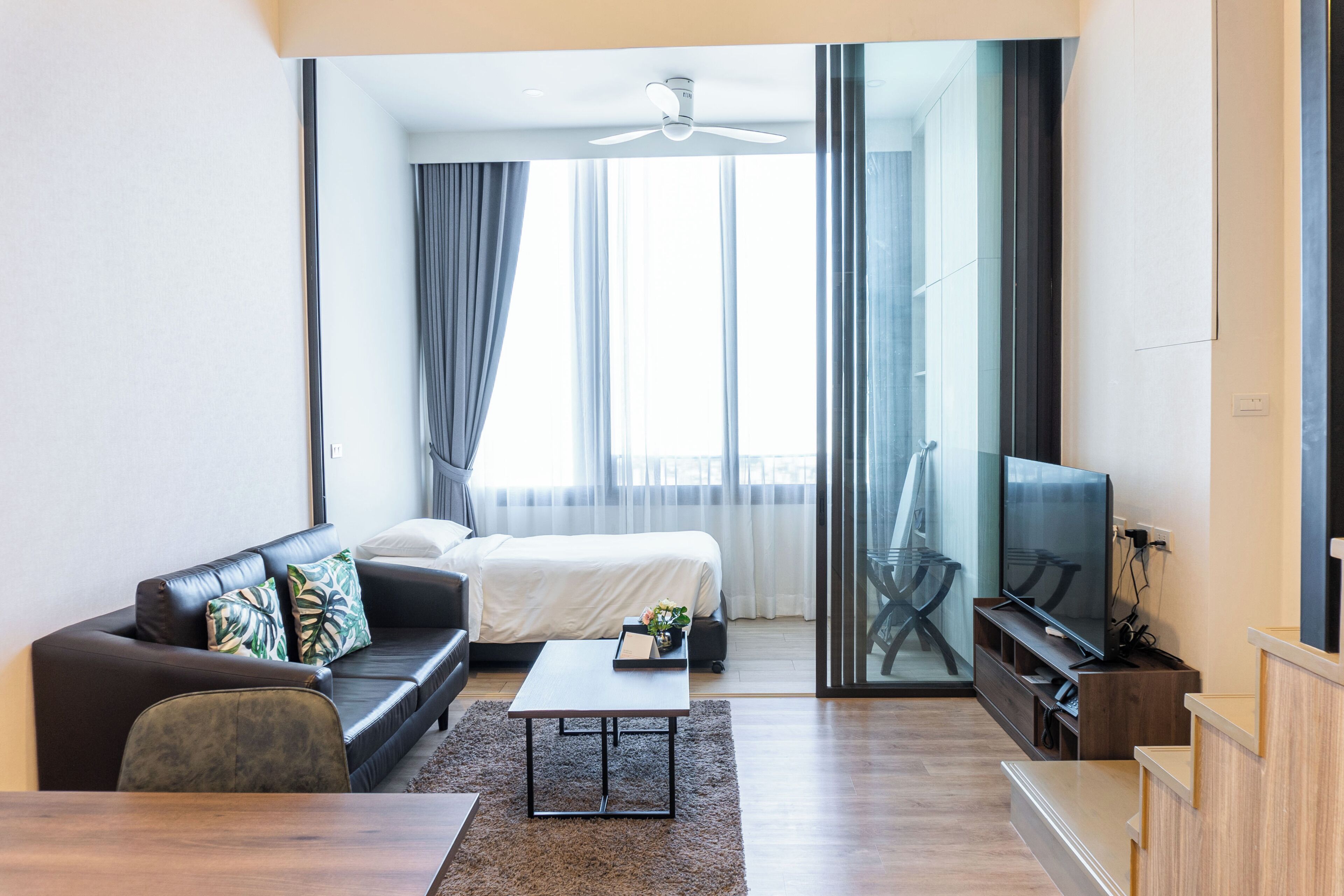 A modern living room with a sofa, coffee table, TV, and a sliding glass door leading to a balcony.