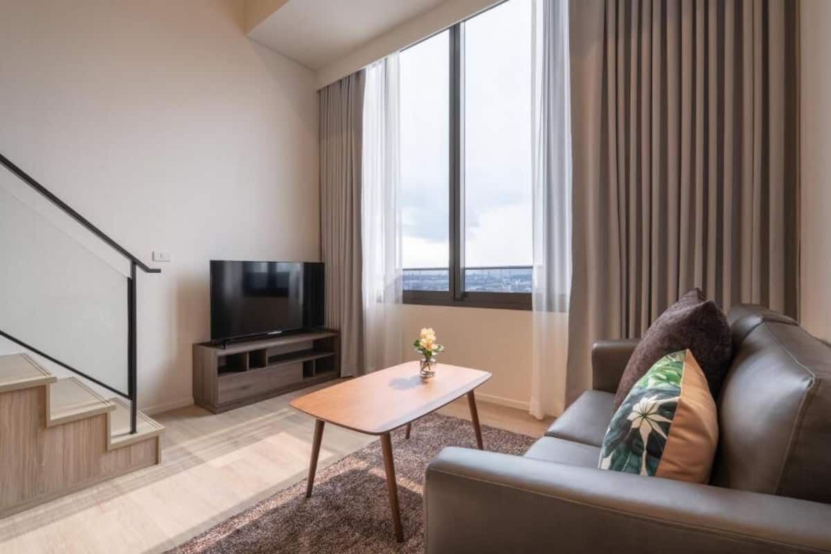 Ett modernt vardagsrum med en platt-TV, en soffa, ett soffbord och en trappa.