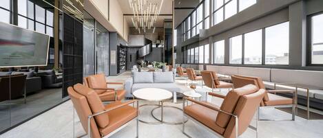 A modern lounge area with leather sofas, round tables, and a large screen displaying a presentation.