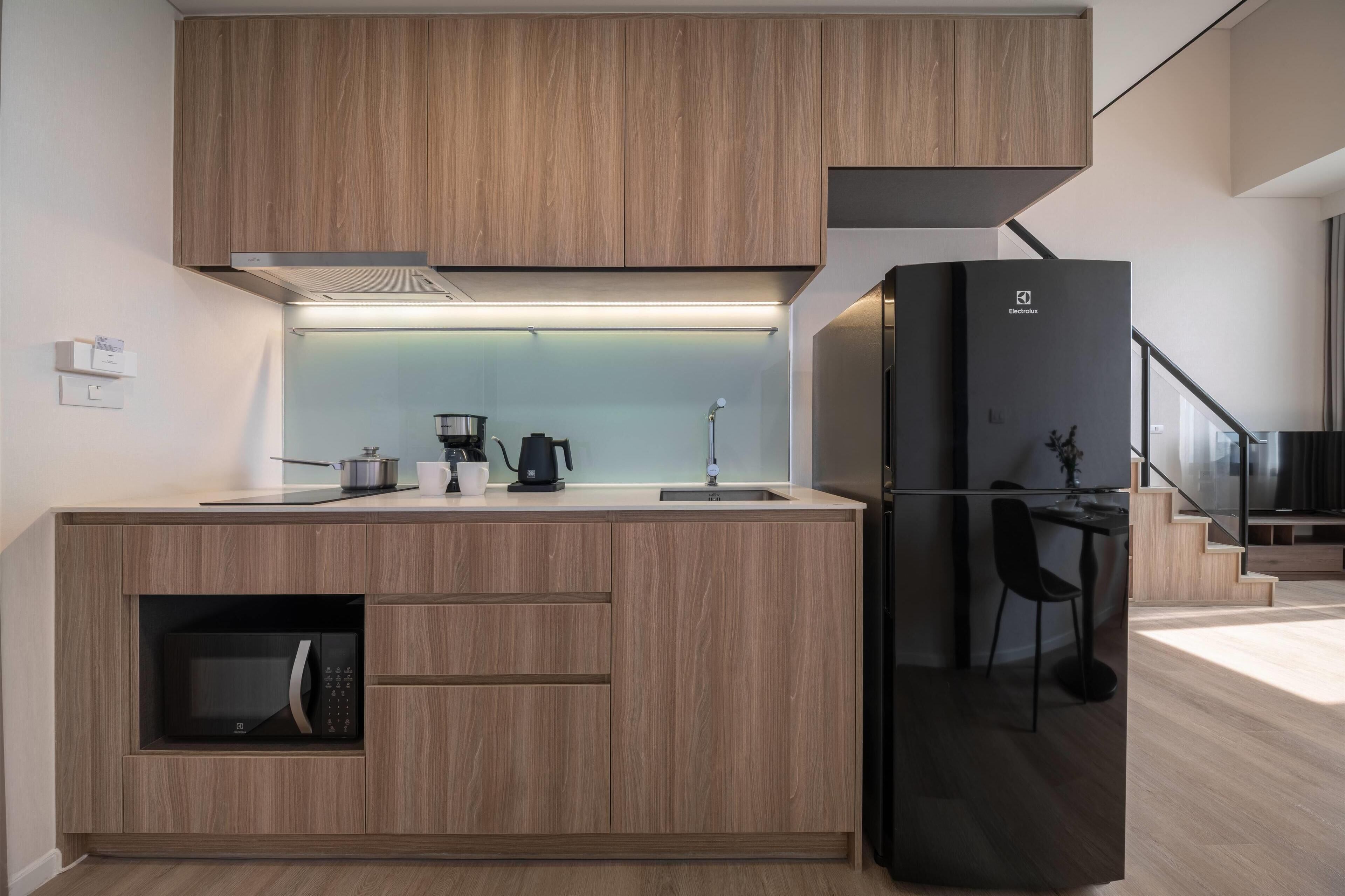 A modern kitchen with wooden cabinets, a black refrigerator, a microwave, a coffee maker, and a sink.